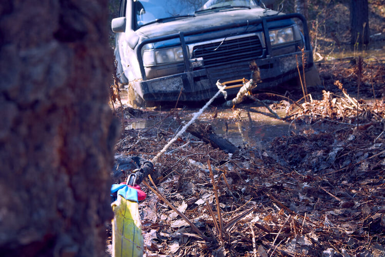 winch line connected to a tree to pull a truck stuck in mud